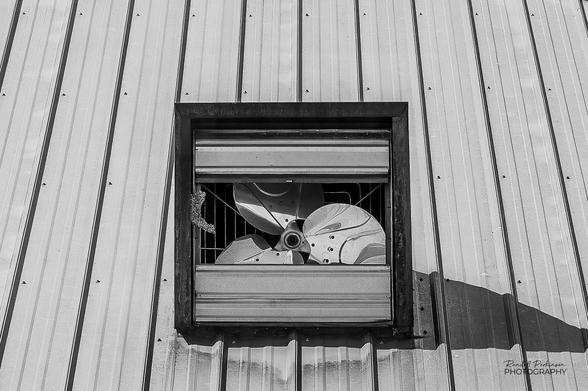 The fan blades of an attic vent fan can be seen through the space where two missing louvers should be.