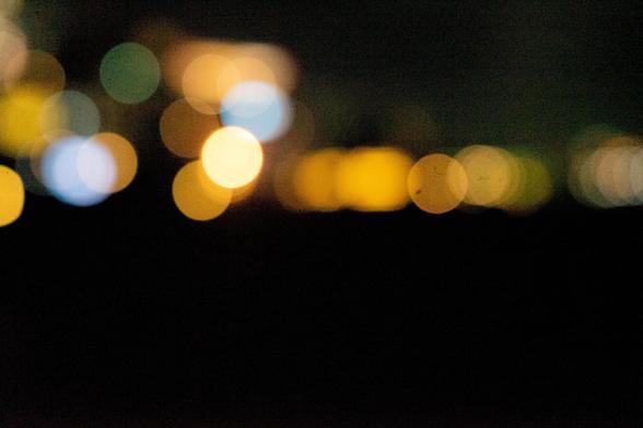 Blurred bokeh lights against a dark background. Circular shapes in various sizes and colors, including yellow, orange, green, and blue, are scattered across the image, creating a soft and abstract appearance.