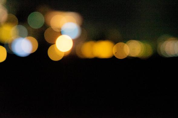 Blurred bokeh lights against a dark background. Circular shapes in various sizes and colors, including yellow, orange, green, and blue, are scattered across the image, creating a soft and abstract appearance.
