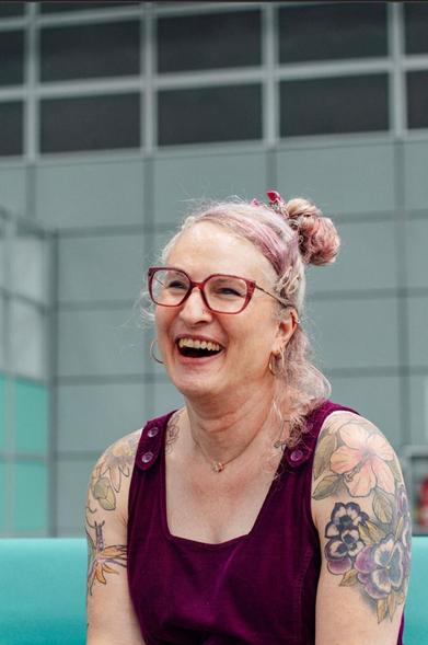 Elodie is laughing with her eyes partly closed
She is wearing a burgundy pinafore dress and pink glasses