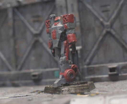 A miniature of a robot, it has two missile launchers on its shoulders and it is rather flat. It looks like it is wearing an apron.