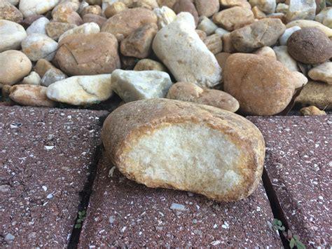 A rock that resembles a small loaf of bread with a big bite taken out of it sitting on a brick border in front of a pile of smaller rocks