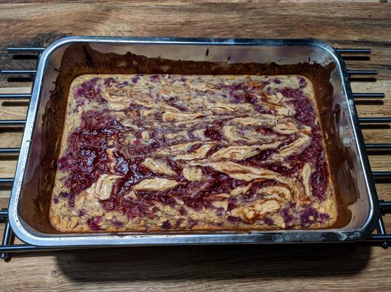 Nieduża forma do pieczenia a w niej pieczona owsianka z kleksami masła orzechowego i dżemu malinowego na wierzchu.