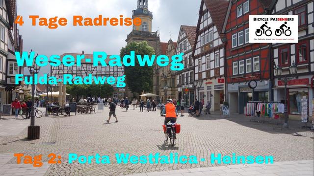 Foto eines Marktplatzes (in Rinteln), auf dem eine Radfahrerin fährt. Rechts mehrere Fachwerkhäuser, dann das Rathaus im Stil der Weserrenaissance, dahinter eine KLirche. Auf dem Marktplatz sind auch viele Menschen unterwegs. Über dem Foto die folg. Schrift: "4 Tage Radreise Weser-Radweg Fulda-Radweg Tag 2: Porta Westfalica - Heinsen".