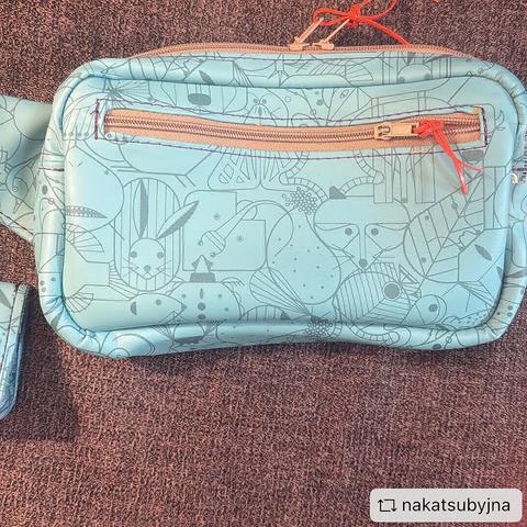 Front of belt bag made from light turquoise Charley Harper animal character print vinyl, with tan zippers, orange zipper pulls, and violet stitching
