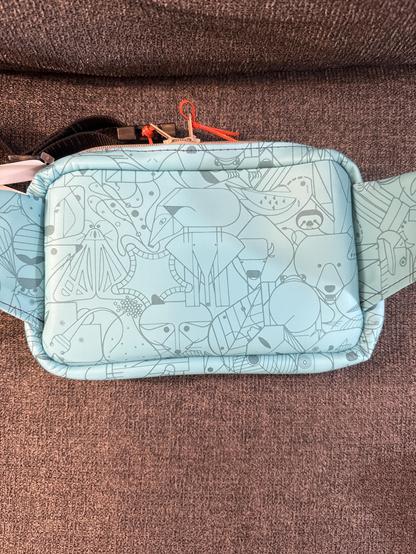Back of vinyl belt bag made from light turquoise Charley Harper print. Tan zippers with orange zipper pulls, and violet stitching