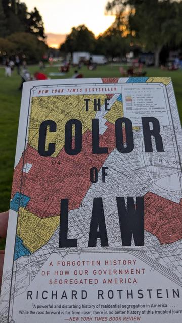 A photo of a book my local public Library gifted me: The color of the law, by Richard Rothstein 

In the background some green grass and a sunset.