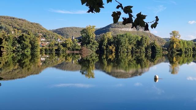 Le plan d'eau de Cajarc sur le Lot , la rive en face se reflète. On devine le causse, la verdure et les toits du village de Salvagnac-Cajarc