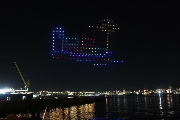 Drones making a picture of a crane and shipping containers.