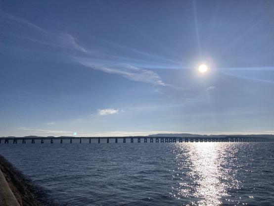 View across Tay Firth towards the rail bridge with the mid morning sun bright overhead shining off the water