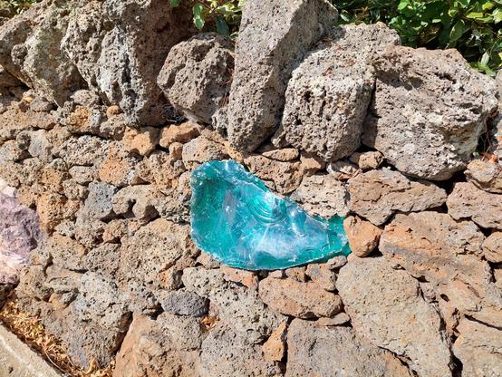 A wall with lots of volcanic rocks and in the middle is a blob of clear blue glass. On the top layer is a row of uneven decorative rocks