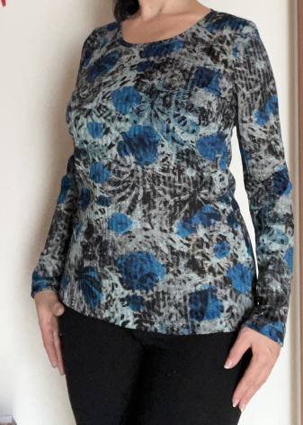 Es ist nur mein Oberkörper zu sehen, ich trage ein selbstgenähtes langärmliges Shirt aus Rippstoff mit einem floralen Muster in blau/schwarz/grau, das Blau dominiert.