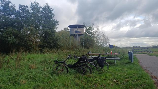 Twee ligfietsen staan geparkeerd bij een picknicktafel bij uitkijktoren de tureluur bij de ackerdijkse plassen . grijze, vlagerige wolken op de achtergrond
