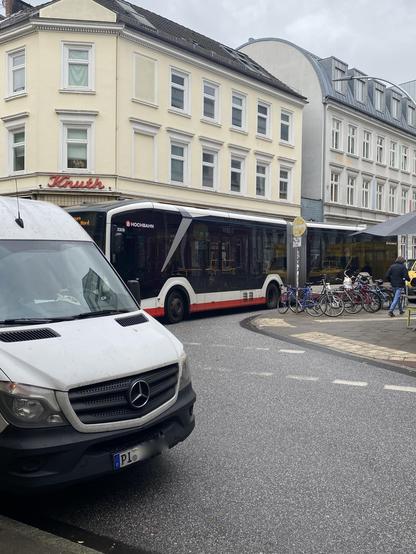 Weißer Sprinter steht im Halteverbot in einer Kurve und blockiert einen Bus - und damit die komplette Straße. Folgende Bilder enthalten diverse Autos und drei weitere wartende Busse.