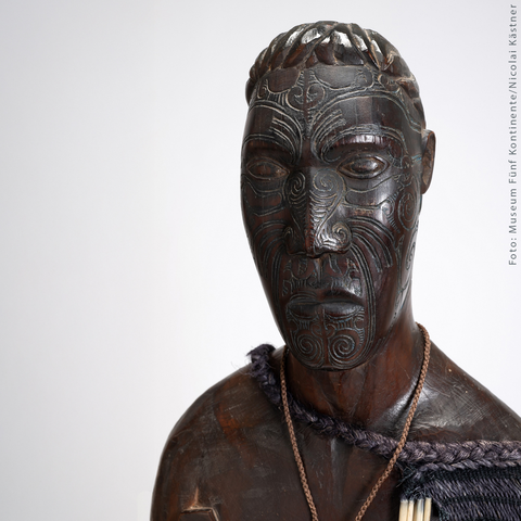 Holzfigur mit Kette um den Hals, dunkle Oberfläche, frontal dargestellt.