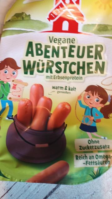 Eine Packung vegane Abenteuerwürstchen auf Erbsproteinbasis. Man sieht fröhliche Kinde auf der Packung. Mit Landkarte, Würstchenlassokette.