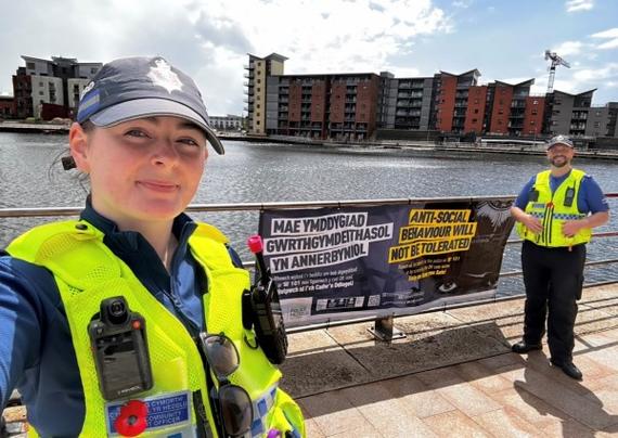PCSOs next to banner reading “Anti‑social behaviour will not be tolerated” in English and Welsh.