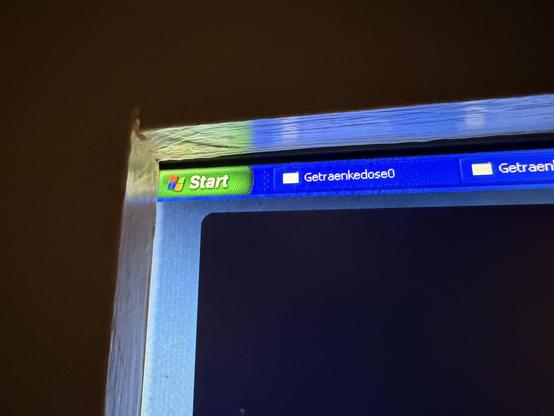 The image shows a close-up of a computer monitor screen, likely displaying a Windows operating system interface. The screen is mostly black, with a light-blue rectangular border around the edges. Along the top edge of the screen, there are several small rectangular icons and text labels. 

Specifically, the text labels read “Start” and “Getraenkdose0”, with a third label appearing partially visible as “Getraenk”. The icons are small and rectangular, and are positioned next to the text labels. The image appears to be taken at a slight angle, and there is some glare on the screen. The monitor itself has a metallic, silver-colored frame.