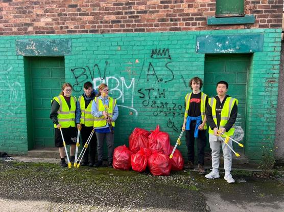 Five young people with litter pickers and rubbish bags standing in front of a graffiti wall in Port Talbot.