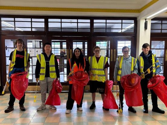 Six young people holding litter pickers and rubbish bags in the lobby of The New Plaza, Port Talbot.