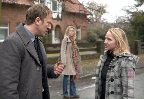 Filmszene aus dem Tatort. Ein Mann spricht mit einer Frau auf einer Dorfstraße. Eine Frau im Hintergrund guckt ihnen zu.