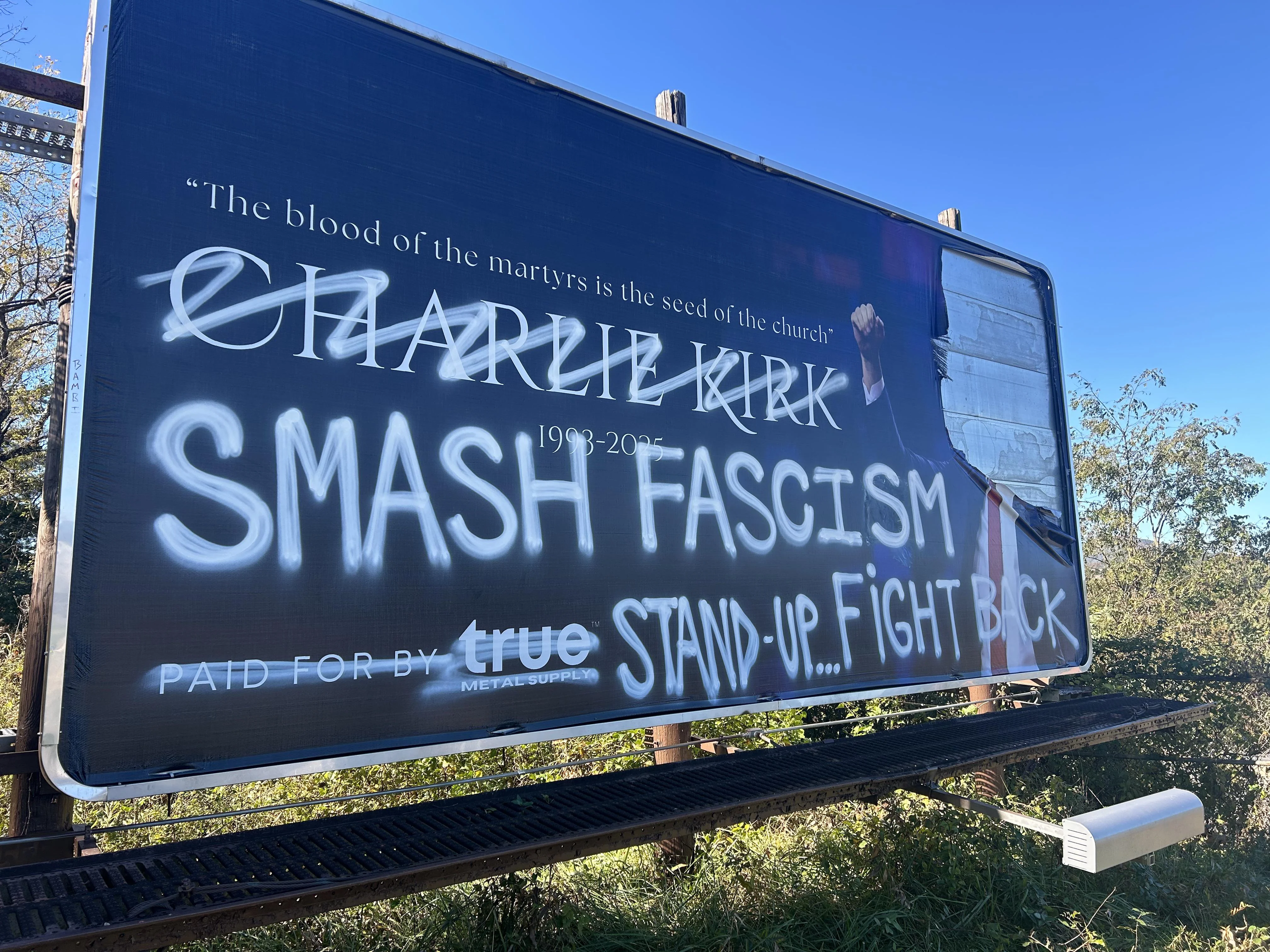 Charlie Kirk billboard in Asheville with Kirk's face ripped down, his name scribbled over and the words "SMASH FASCISM" AND "STAND UP... FIGHT BACK" graffitied in white paint