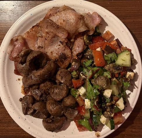 A photograph of my dinner. A white plate on a wooden table, tasty meatses on the left, colourful plants on the right, mostly green and red. It glistens with artery-blocking fat that my doctor would berate me for most sternly, but it's tasty enough that if he were to get even the slightest whiff of it, never mind see it or taste it, he would forswear forever his healthy lifestyle.