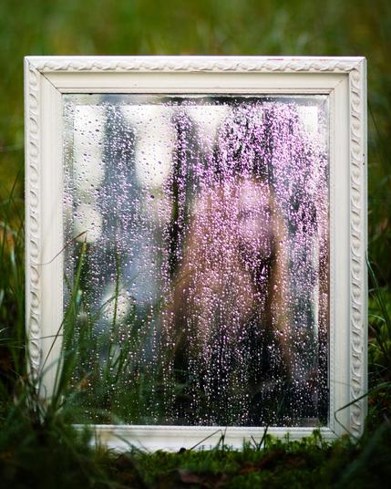 a blurry reflection of a woman in antique mirror in a forest
