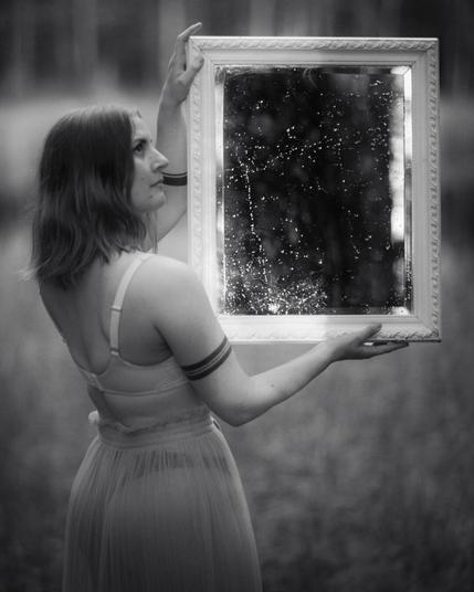 a woman holding an antique mirror in front of a pond