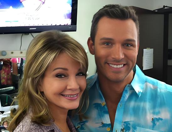Behind-the-scenes photo from the Days of Our Lives set, likely late 2008, featuring actors Deidre Hall (Marlena Evans) and Eric Martsolf (Brady Black). They are standing close together, smiling directly at the camera. Deidre wears a light brown patterned jacket, and her blonde hair is softly waved around her face. Eric wears a light blue and white button-down shirt with a casual, summery print. The background appears to be the make-up room, with a wall-mounted TV, a mirror framed with round bulbs, and shelves visible. The image conveys a warm, candid moment between two iconic soap stars known for their roles in Salem’s most dramatic storylines.