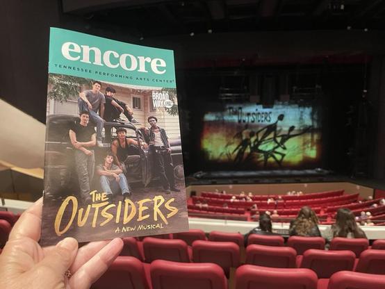 Playbill with actors on, in, and around a black pickup, and the curtain with show logo. A few folks arrived early like we did, but most of the plush red seats are empty