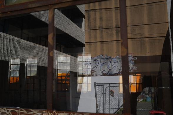 View through a window with windows visible on the other side backlight by the sun. A gate and graffiti are reflected in the nearest windows.