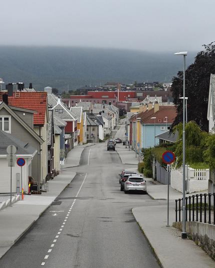 A photo looking down a long street with sidewalks on both sides and a bike lane. There are houses of many colors along the street and some parked cars. There is a large hill in the distance that disappears into cloud.
