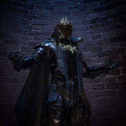 This image depicts a dramatic figure in ornate, dark armor standing in a commanding pose against a textured stone wall. The armored figure wears an elaborate helmet with a pointed crest and is clad in intricate medieval-style armor that appears metallic with blue-tinted highlights. A flowing cape or cloak drapes from the shoulders, and the armor features detailed decorative elements throughout, including ornate patterns on the chest plate and leg guards.
The figure stands with arms outstretched in a triumphant gesture. The scene is atmospherically lit by multiple melted candles arranged in two groups on the floor—three on the left side and three on the right side of the figure. The candles cast a warm, flickering glow that contrasts beautifully with the cool blue tones of the armor and the dark, shadowy stone wall backdrop. The overall composition creates a mystical, gothic atmosphere reminiscent of dark fantasy or medieval settings.