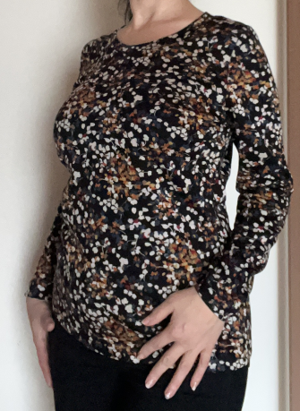 Zu sehen ist mein Oberkörper, ich trage ein selbstgenähtes langärmliges Shirt mit einem kleinen abstrakten Blumenmuster. Der Stoff ist schwarzgrundig, die "Blumen" beige, weiß, hellbraun mit ein bisschen rot und blau.