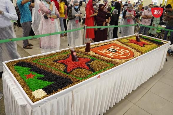 A large, rectangular table with a white tablecloth holds a colorful mosaic made of dried fruits and nuts.
