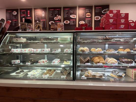 A pastry shop with display cases full of cakes, pastries, and doughnuts. Menu boards are visible in the background.