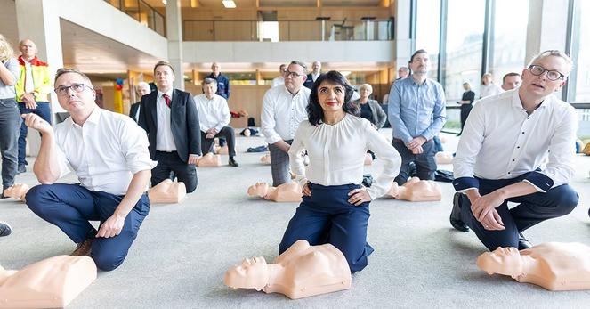 Abgeordnete kniend vor den Puppen beim Üben der Herzdruckmassage