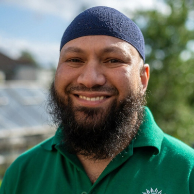 Mothin smiling to camera.  Wearing an open collared Green Party tee shirt and blue  kufi.