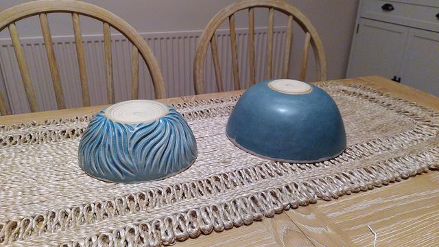 Two bowls upside down on a table, one carved with organic lines and glazed in glossy ice-blue, the other in dark matt blue green.