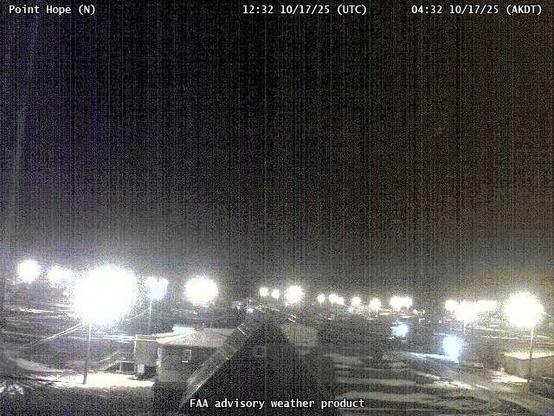 A webcam overseeing a beach with an ocean view, with a few small buildings and utility poles.