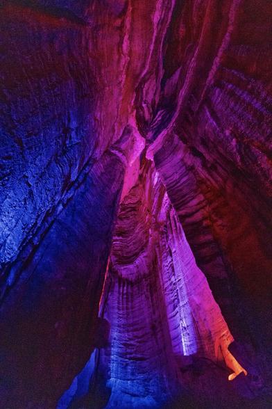 A vertical view inside Ruby Falls cave, with purple and pink lights illuminating tall stone walls that seem to stretch endlessly upward. The atmosphere feels mystical, almost like a fantasy game setting.