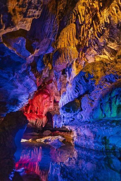 Reflections of red and violet lights shimmer on wet cave walls at Ruby Falls, creating a mirror-like effect that blends water and rock into abstract shapes