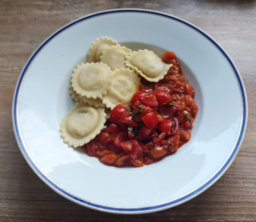 Das fertige Gericht mit Tomatensauce, darauf frische Tomaten, mit Ravioli auf dem Teller