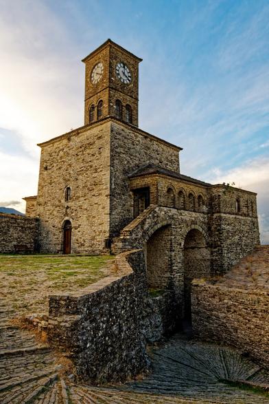A castle made of bricks with a dominant clocktower on the top and a winding, narrow road made of stone plaster.