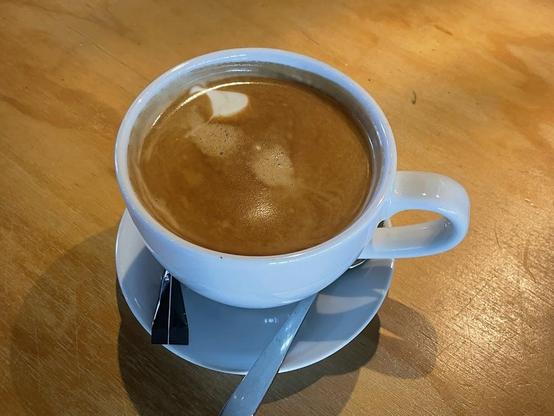 A cup of coffee on a saucer sits on a wooden table.