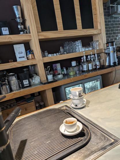 Here are three coffee cups on saucers in a cafe setting. Two are stacked, and one is an espresso cup with a spoon.