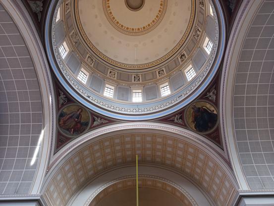 Foto der Nikolaikirchen-Kuppel in Potsdam, von innen. 

Der Blick geht von unten nach schräg oben. Zu sehen sind "Kreise", "Halbkreise" und Bögen. Das sind die verkleideten Gewölbebögen und die Kuppel im Innenraum der Kirche St. Nikolai in Potsdam. Am Kuppelrand sind christliche Bilder mit Teilbereichen in Gold. Die Kuppel hat in regelmäßigen Abständen kleine Fenster.