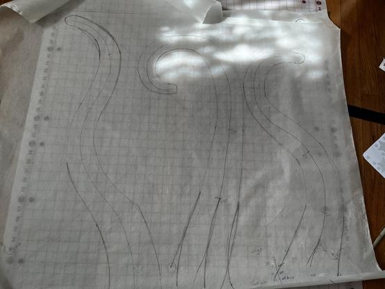 A large sheet of paper is laid over a gridded cutting mat. Three very large tentacles (each about 1 yard long) have been sketched out on it.  The tentacles are all wiggly in different directions.