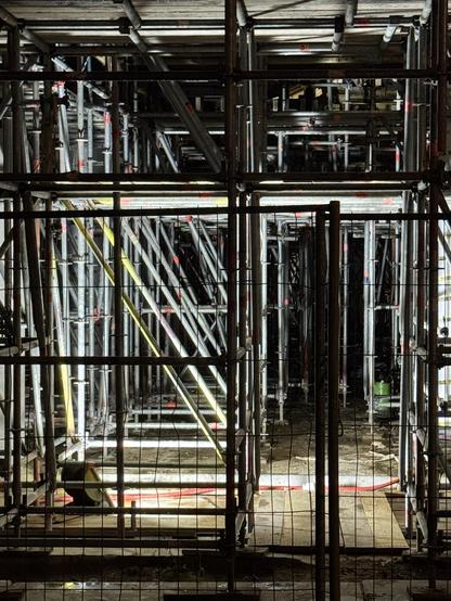 Schützendes Gestänge bei einem Neubau. Das Dunkel, und einige der Stahl streben werden hell erleuchtet.